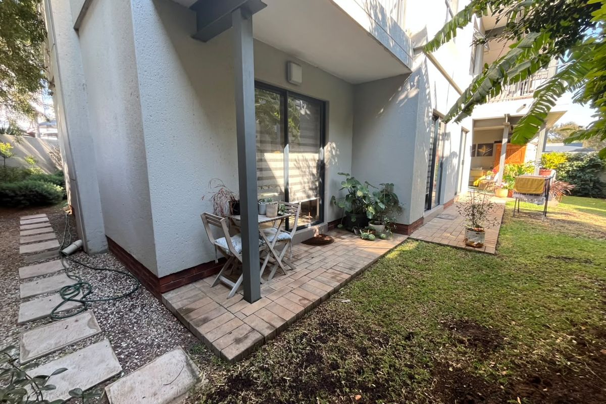 A rear exterior view of the apartment featuring a paved patio area, sliding glass doors, and access to a private garden space.