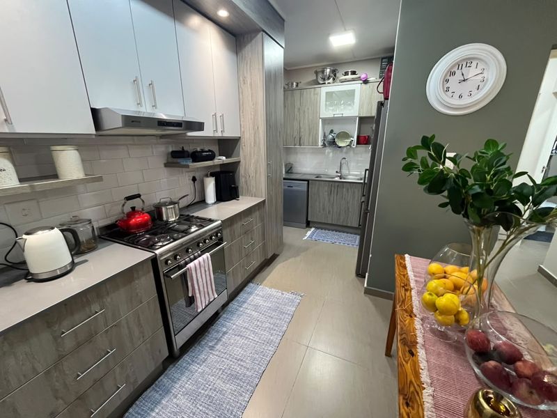 Modern kitchen featuring wood-grain cabinetry, gas stove with extractor fan, tiled backsplash, and integrated dishwasher, offering a functional and contemporary cooking space.