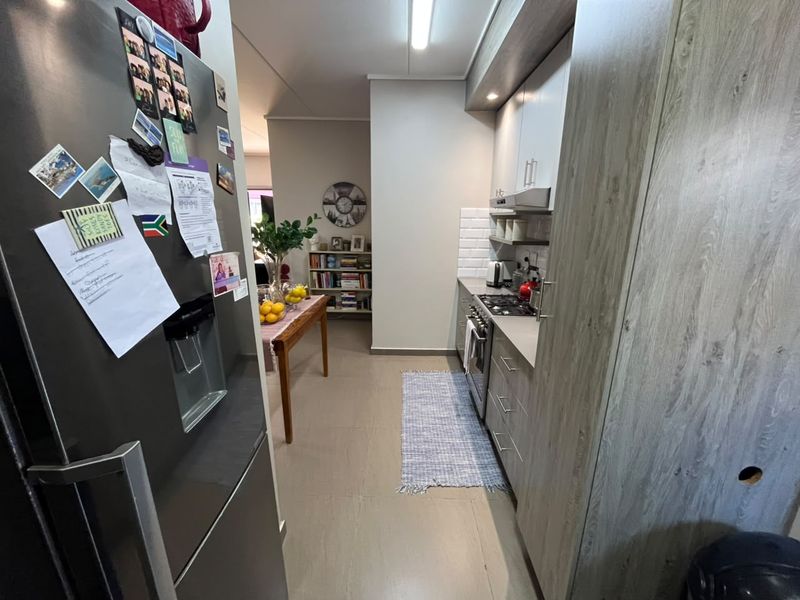 A functional galley-style kitchen featuring modern wood-look cabinetry, a gas hob, oven, extractor fan, and a classic white subway tile backsplash.