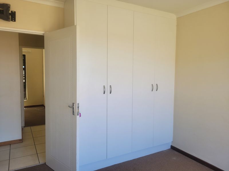A clean, empty bedroom featuring built-in cupboards, neutral wall finishes, and carpeted flooring, offering a blank canvas for personalization.