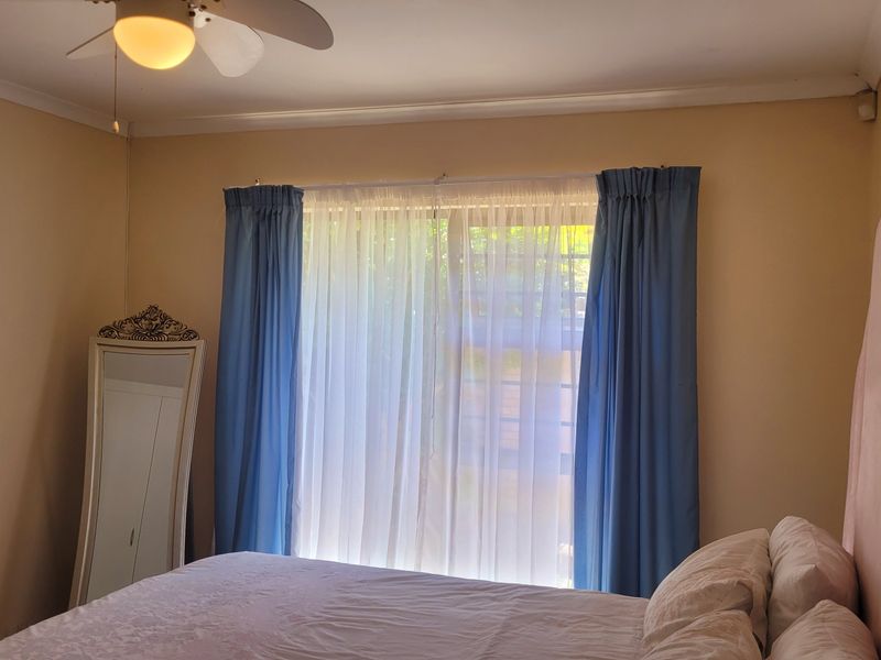 A bedroom featuring a ceiling fan, coving, and a window with curtains, providing a functional and comfortable living space.