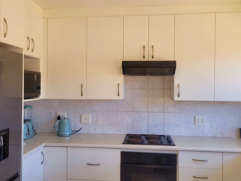 A functional kitchen featuring white cabinetry, laminate countertops, a tiled backsplash, and integrated cooking appliances including an electric hob and oven.
