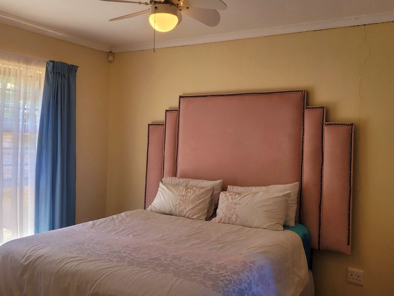 A bedroom featuring a ceiling fan and a sliding door providing natural light, with visible wall cracking requiring maintenance.