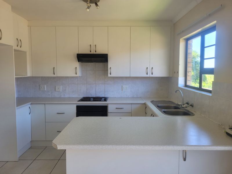 A functional kitchen featuring white cabinetry, laminate countertops, a built-in oven with hob, and a double bowl sink with tiled backsplash.