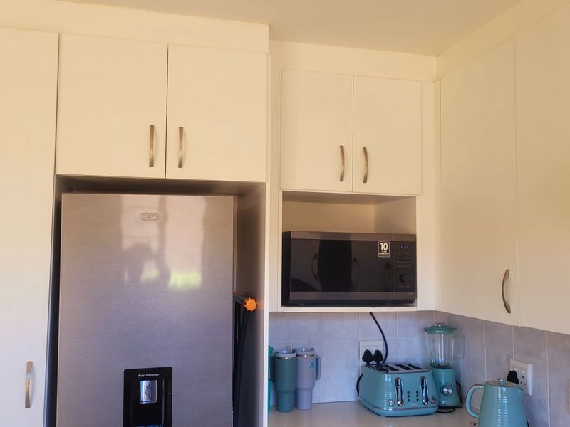 A functional kitchen area featuring white built-in cabinetry, a tiled backsplash, and an integrated extractor fan above the workspace.