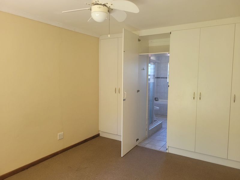 A spacious bedroom featuring built-in cupboards, a ceiling fan, and direct access to an en-suite bathroom.