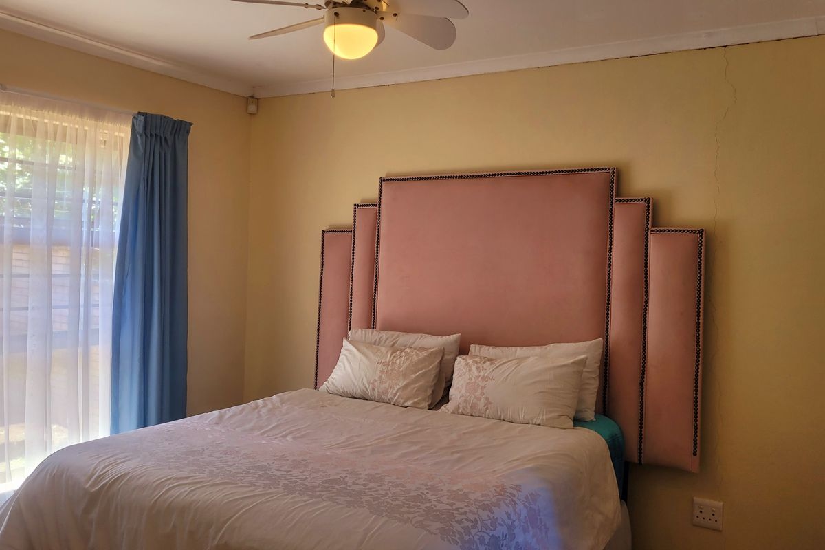 A bedroom featuring a ceiling fan and a sliding door providing natural light, with visible wall cracking requiring maintenance.