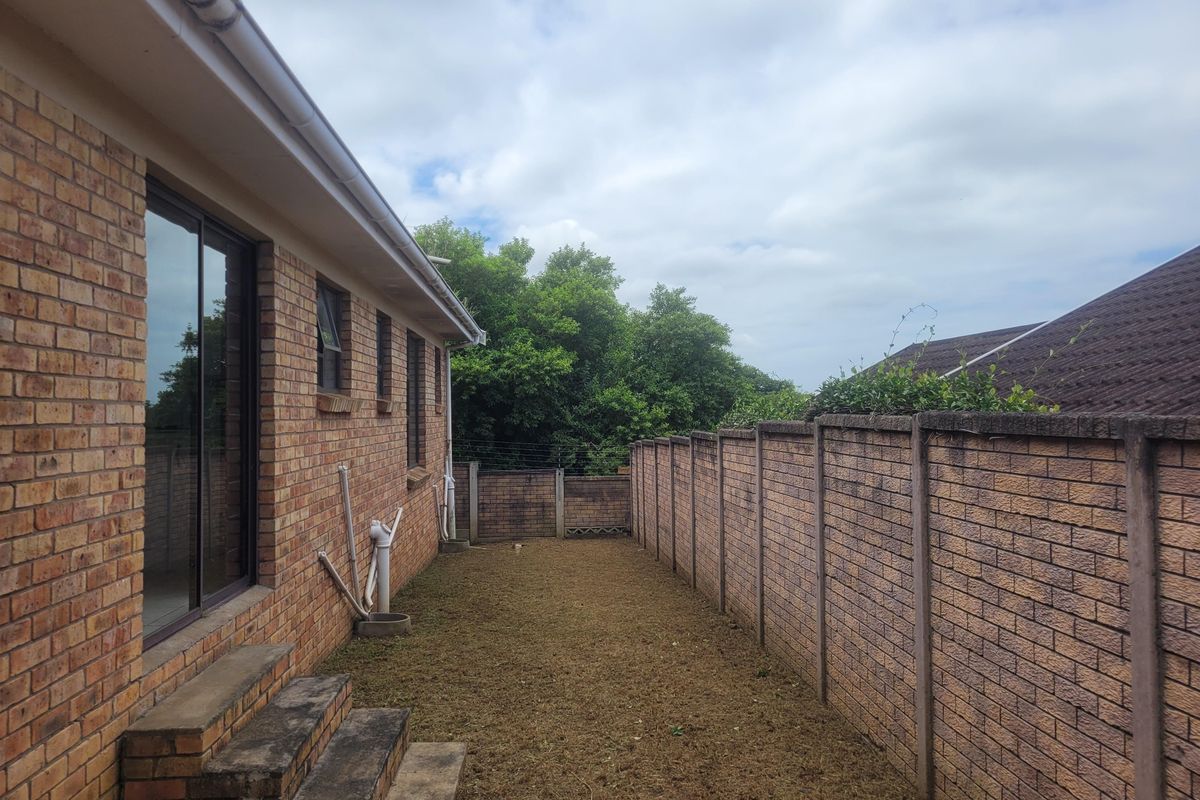 A private rear garden area featuring a brick townhouse facade, sliding door access, concrete steps, and a secure precast boundary wall with electric fencing.