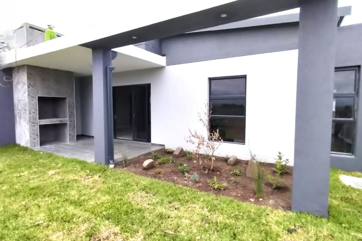 A modern rear exterior view featuring a covered patio with a built-in braai, aluminium sliding doors, and a landscaped garden area.