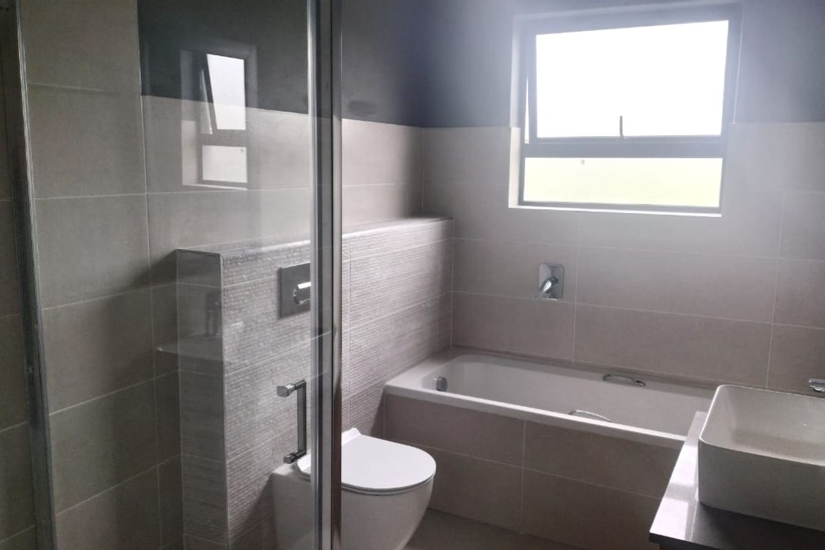 Modern bathroom featuring a glass shower enclosure, wall-hung toilet, built-in bathtub, and a contemporary countertop basin with neutral wall tiling.