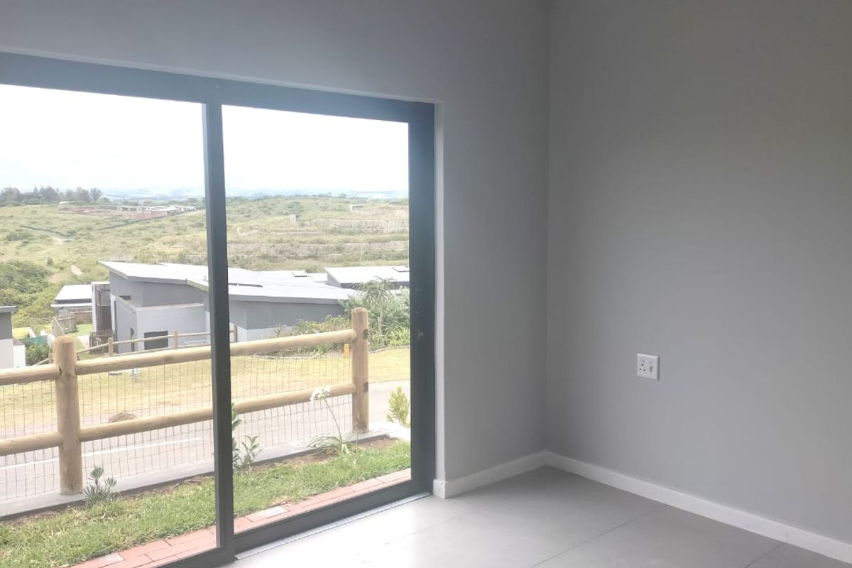 A bright, empty bedroom featuring modern tiled flooring and a large sliding glass door that opens to a scenic outdoor view.