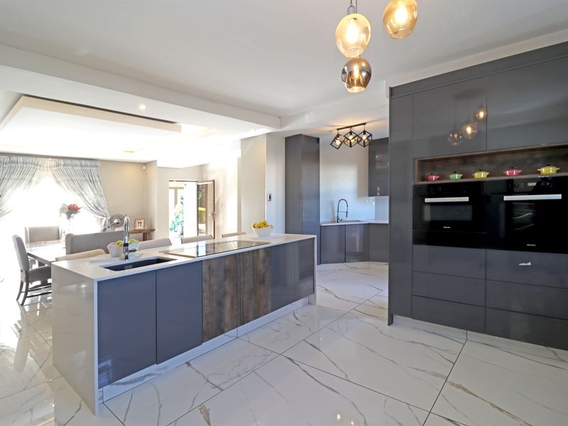 Modern open-plan kitchen featuring a central island, high-gloss cabinetry, integrated appliances, and premium marble-look floor tiles, seamlessly flowing into the dining area.