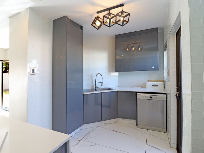 A modern, well-lit scullery featuring sleek grey cabinetry, white subway tile backsplash, marble-look floor tiles, and a stainless steel sink.