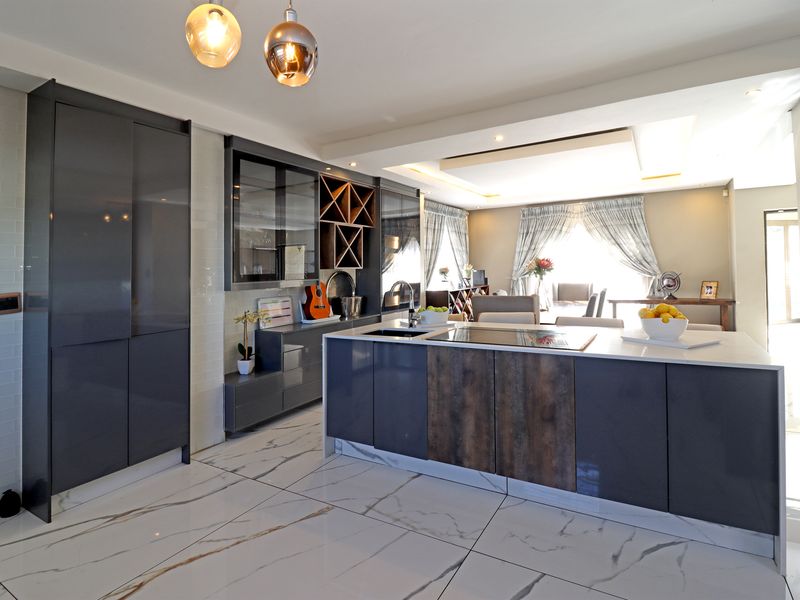Modern open-plan kitchen featuring high-gloss cabinetry, a central island with integrated cooktop, and elegant marble-look floor tiles flowing into the living area.