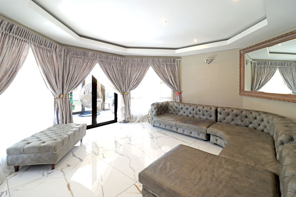 Spacious living room featuring polished marble-look floor tiles, a modern recessed ceiling with downlights, and large sliding glass doors providing access to the patio.