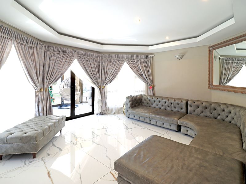 Spacious living room featuring polished marble-look floor tiles, a modern recessed ceiling with downlights, and large sliding glass doors providing access to the patio.