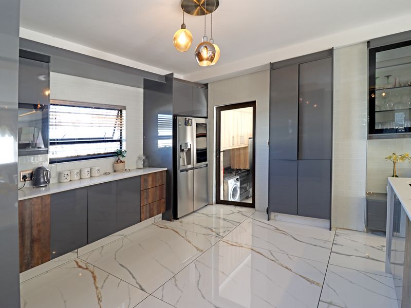 Modern kitchen featuring high-gloss grey cabinetry, marble-look floor tiles, subway tile backsplash, and elegant pendant lighting, with an adjacent scullery area.