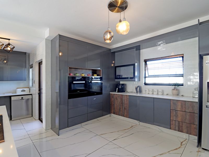 Modern kitchen featuring high-gloss grey cabinetry, wood-look accents, marble-effect floor tiles, subway tile backsplash, and integrated stainless steel appliances.