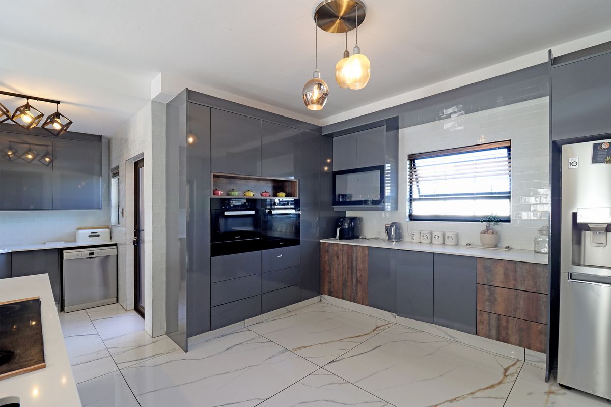 Modern kitchen featuring high-gloss grey cabinetry, wood-look accents, marble-effect floor tiles, subway tile backsplash, and integrated stainless steel appliances.