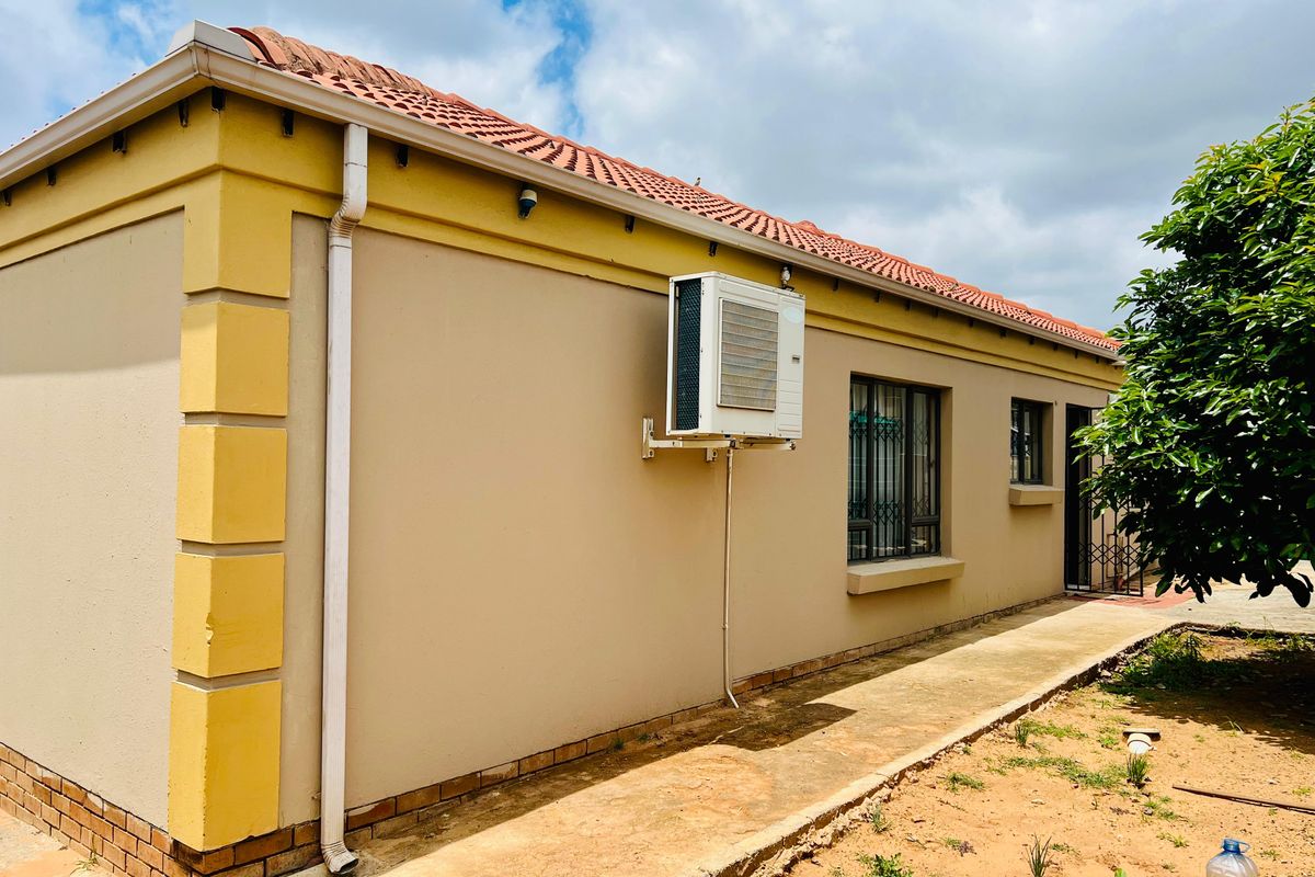 Rear exterior view of the townhouse featuring a tiled roof, concrete pathway, and wall-mounted air conditioning unit with security bars on the windows.
