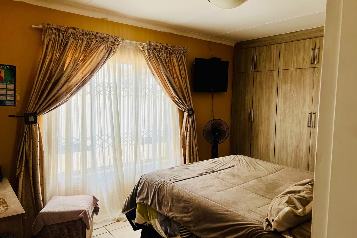 A functional bedroom featuring built-in wooden cupboards, tiled flooring, and a large window with security gate access.