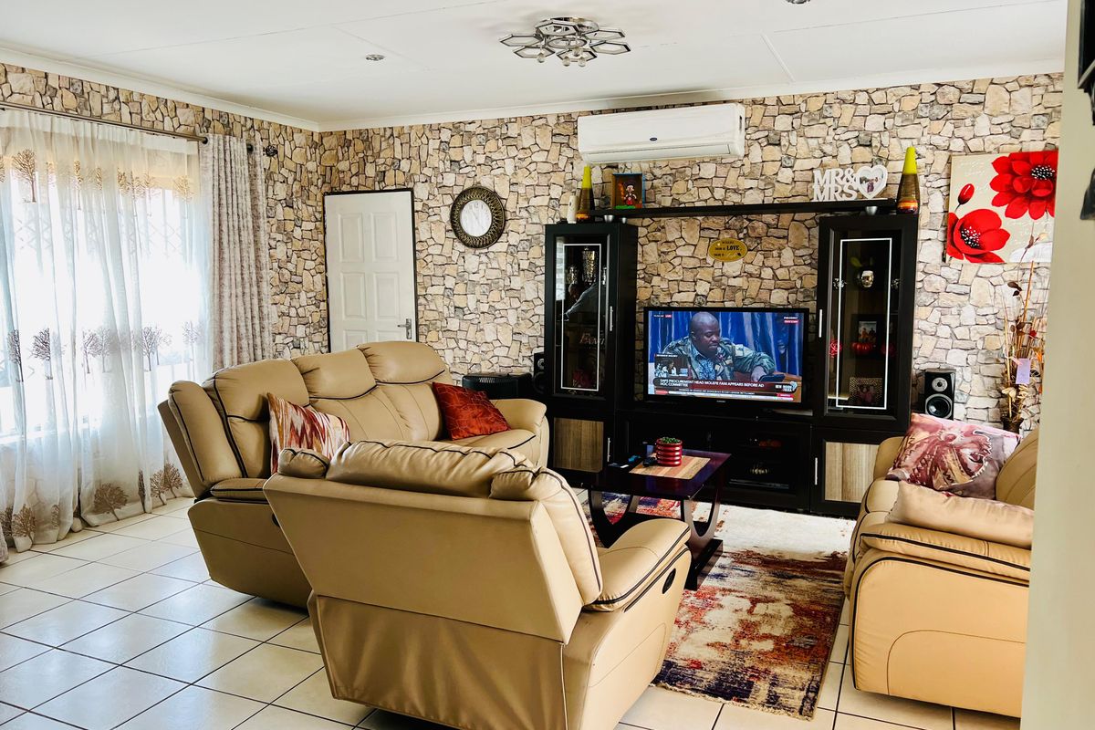 A comfortable living room featuring a distinctive stone-cladding accent wall, tiled flooring, and a wall-mounted split-system air conditioner.