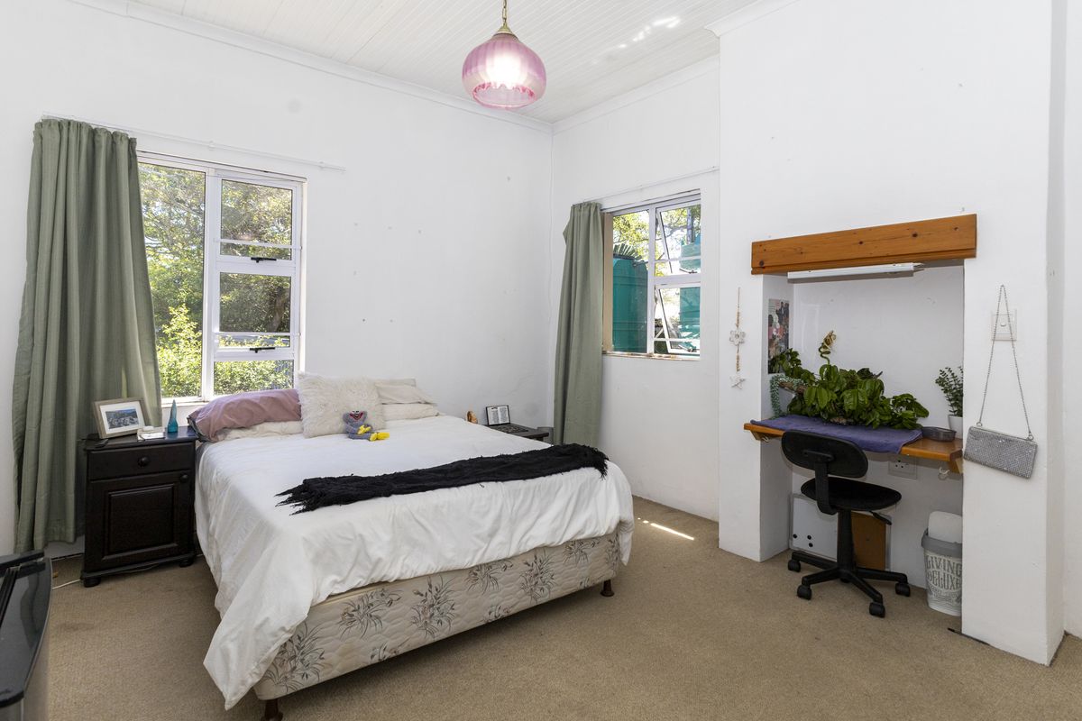A bedroom featuring a built-in desk area, timber shelving, and aluminium windows, with neutral wall finishes and carpeted flooring.