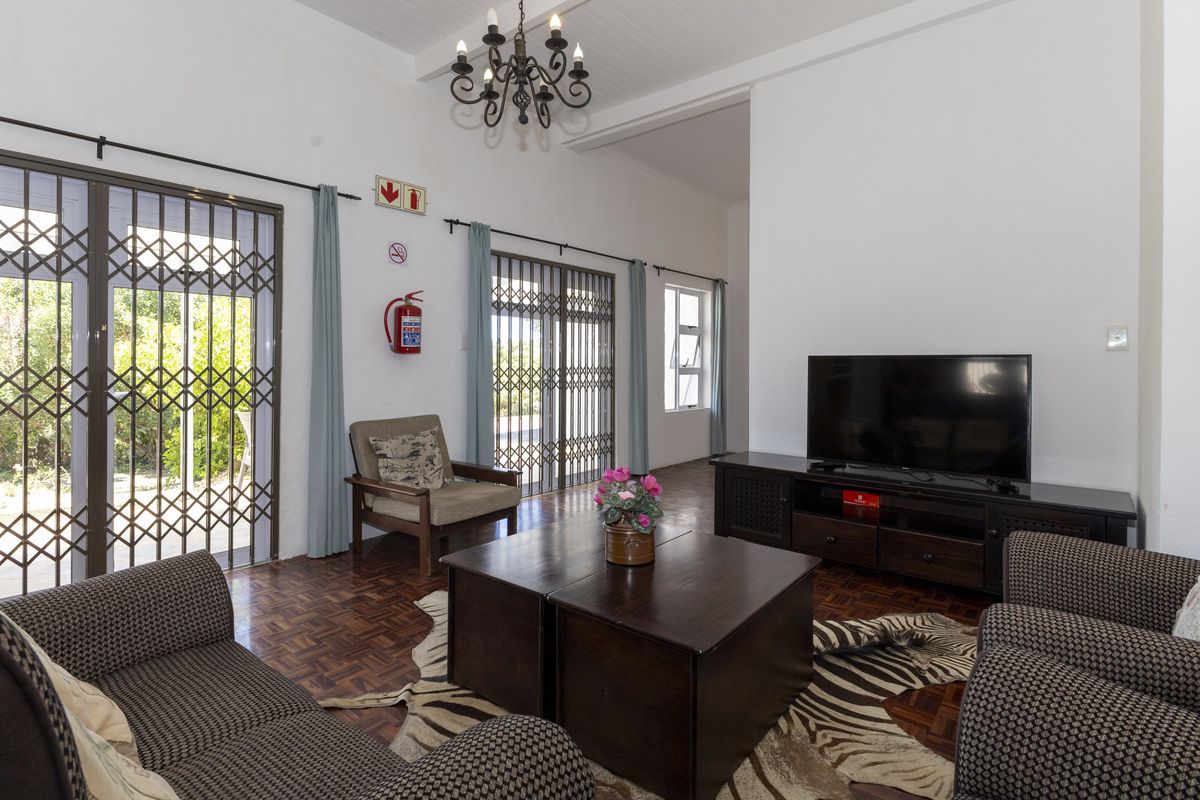A living room featuring classic parquet flooring, wrought iron chandelier lighting, and direct access to the garden through secure metal sliding doors.