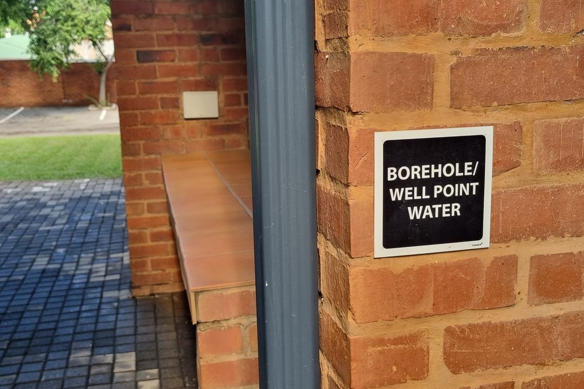 An outdoor area featuring brick masonry, a tiled bench, and a borehole water supply point.
