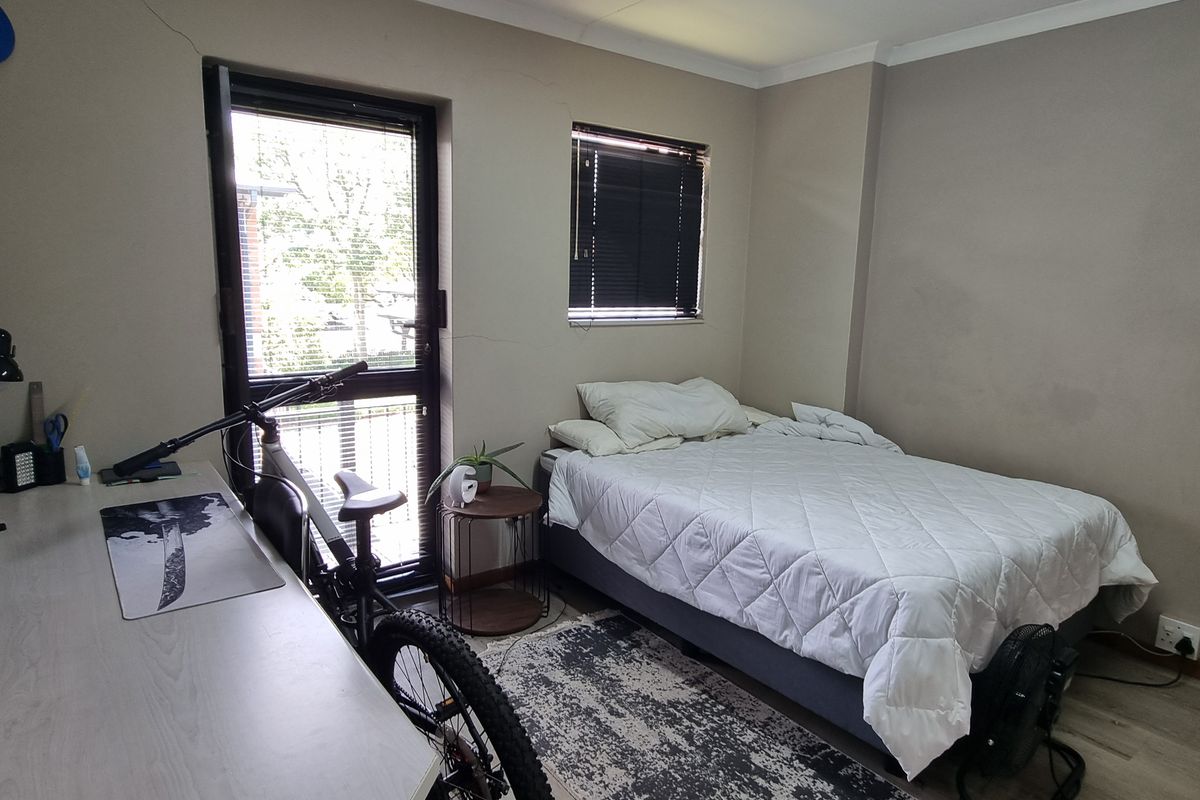 A bedroom featuring laminate flooring, built-in shelving, and aluminium window and door frames, showing signs of wall cracking.