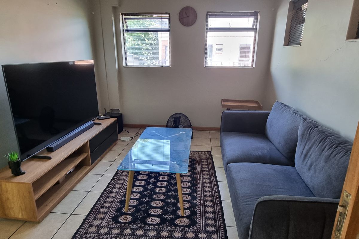 A functional living room featuring tiled flooring and natural light through multiple windows, providing a comfortable space for relaxation.
