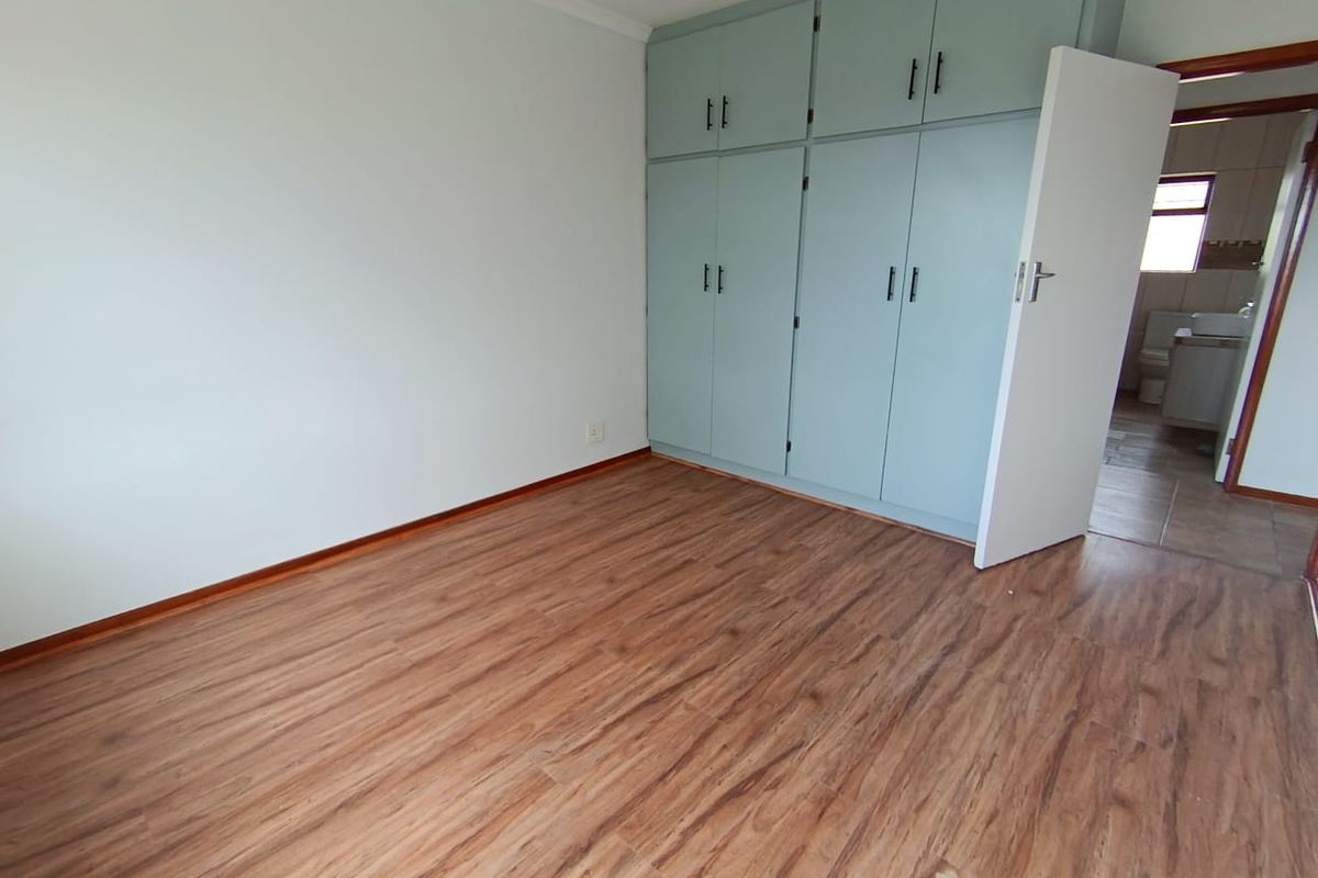 A bright bedroom featuring wood-look laminate flooring and built-in cabinetry, with an open doorway leading to an adjacent bathroom.