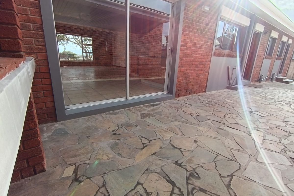 A rear patio area featuring natural stone paving, red brick exterior walls, and large sliding glass doors leading into the interior living space.