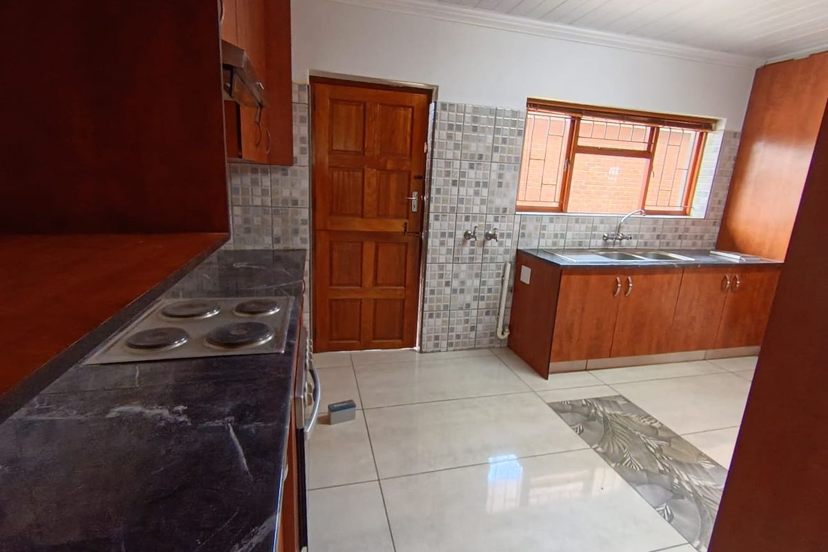 Functional kitchen featuring wooden cabinetry, dark stone-look countertops, built-in electric hob, and tiled flooring with a decorative inlay.