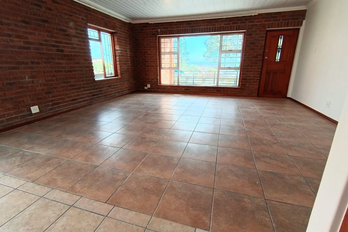 Spacious living area featuring exposed brick walls, large windows with natural light, and durable tiled flooring throughout.
