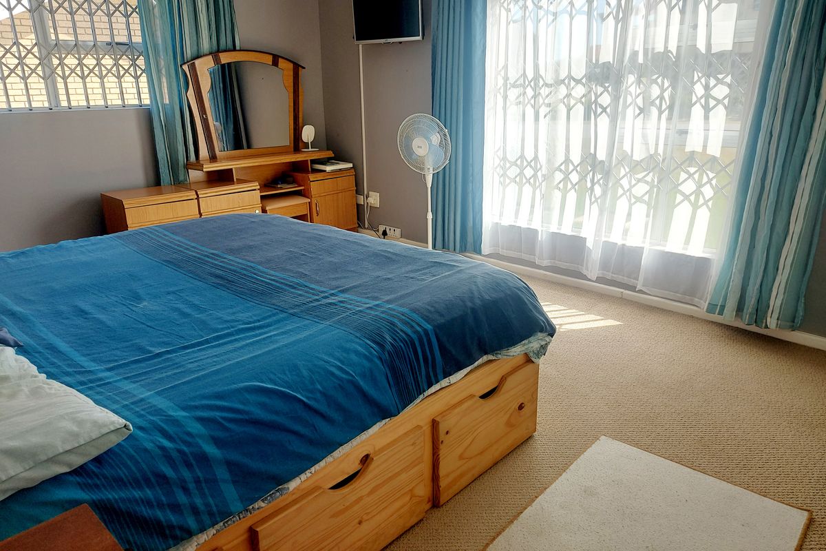 A well-lit bedroom featuring neutral carpeting, large windows with security gates, and ample natural light.