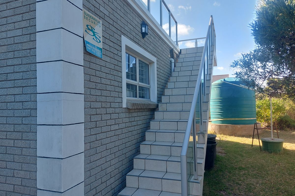Exterior view of the property featuring a tiled staircase leading to an upper level with glass balustrades and a water storage tank in the garden.
