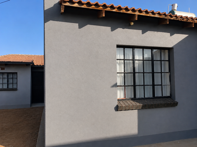 Rear exterior view of the property featuring grey rendered walls, terracotta roof tiles, and steel-framed grid windows with a solar water heater installed.