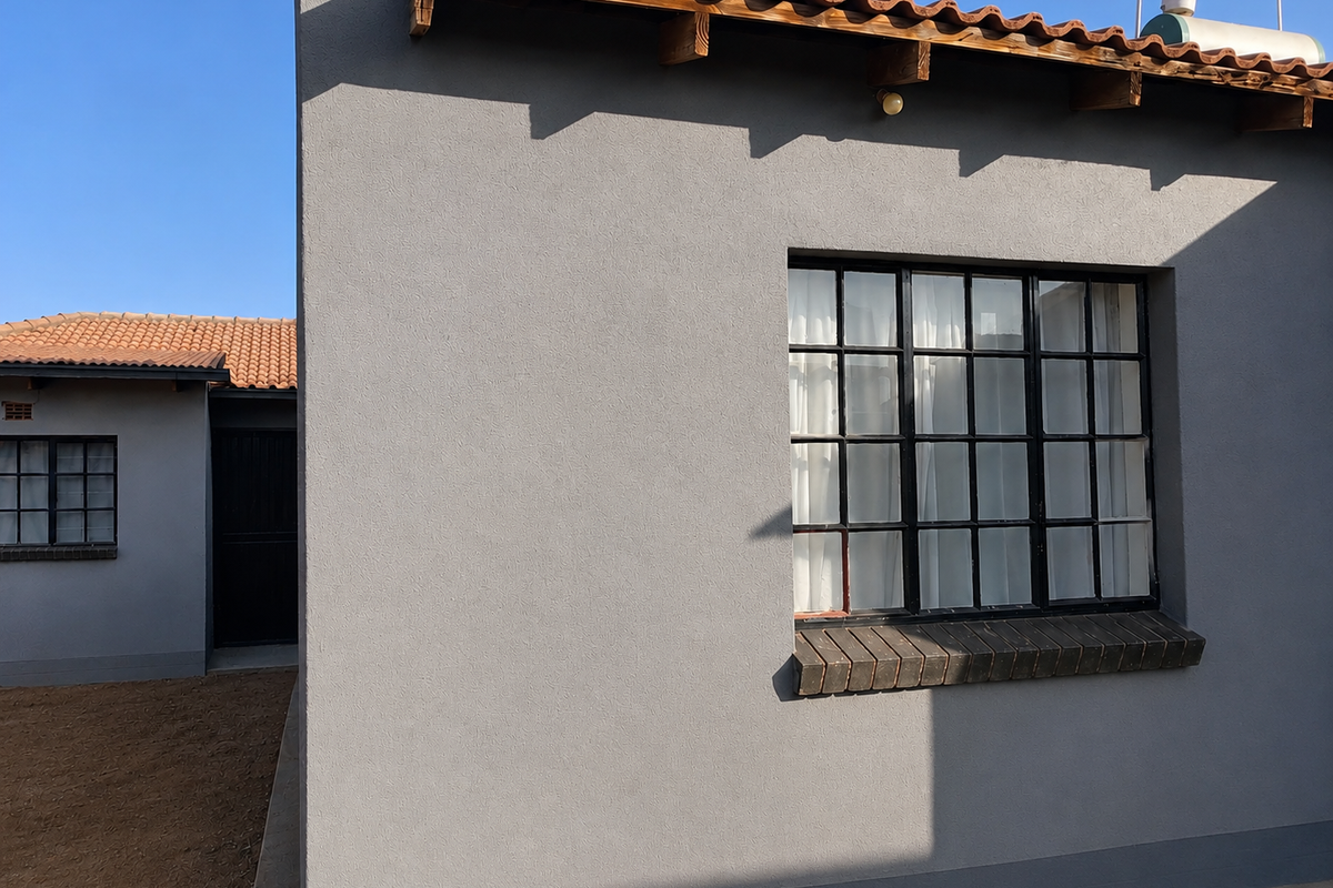 Rear exterior view of the property featuring grey rendered walls, terracotta roof tiles, and steel-framed grid windows with a solar water heater installed.