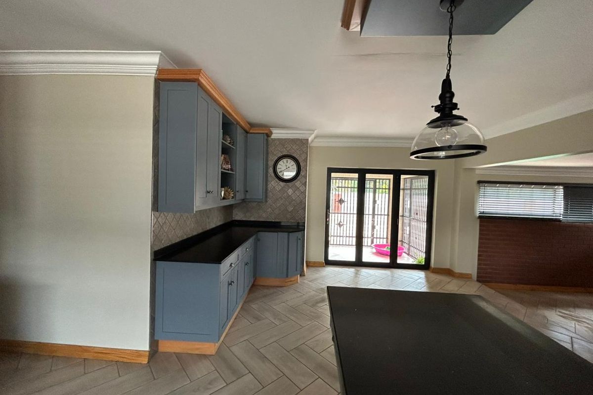 A modern kitchen featuring blue cabinetry, dark stone countertops, herringbone tile flooring, and direct access to an outdoor area through sliding glass doors.