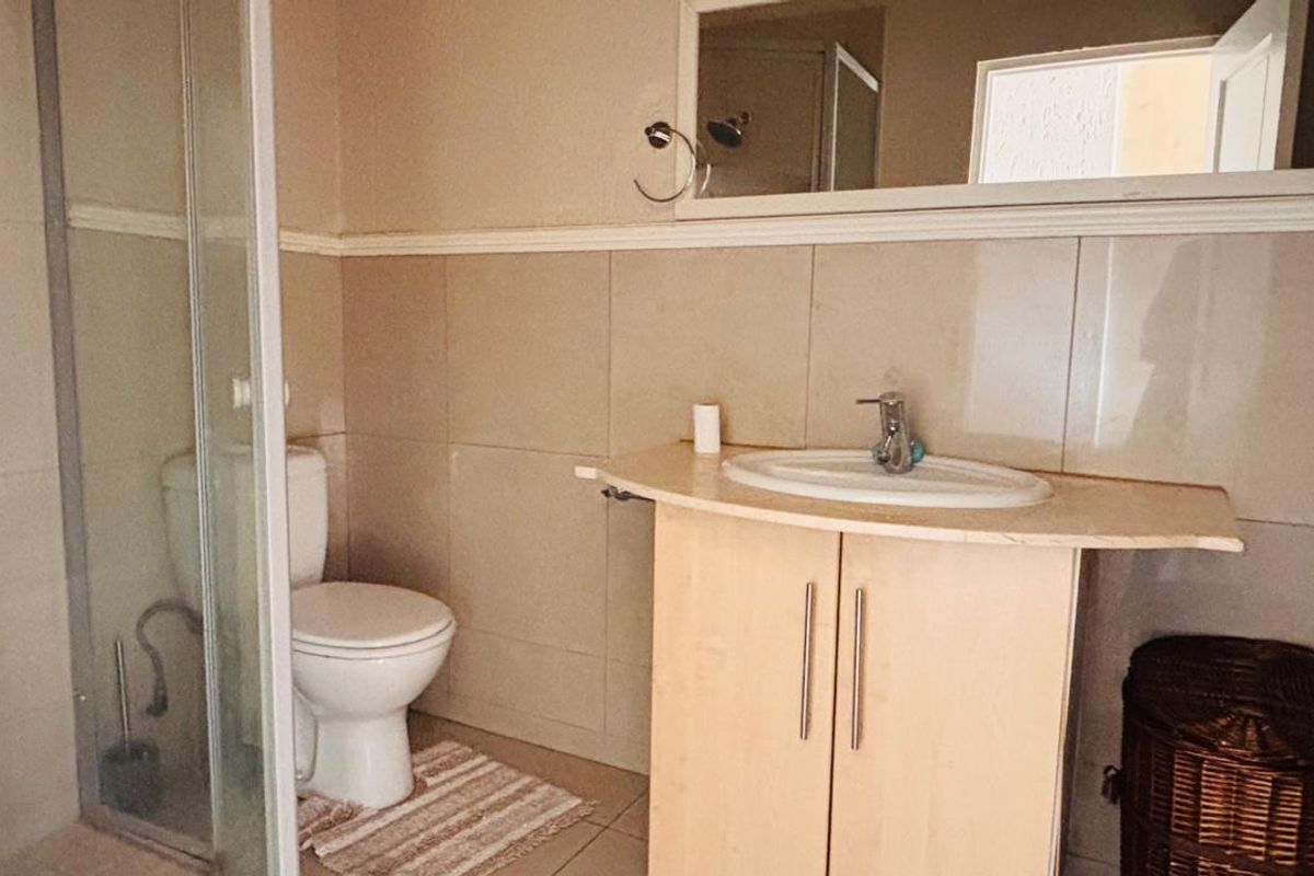 A functional bathroom featuring a shower enclosure, a vanity cabinet with a washbasin, and wall-mounted mirror with neutral tiled finishes.
