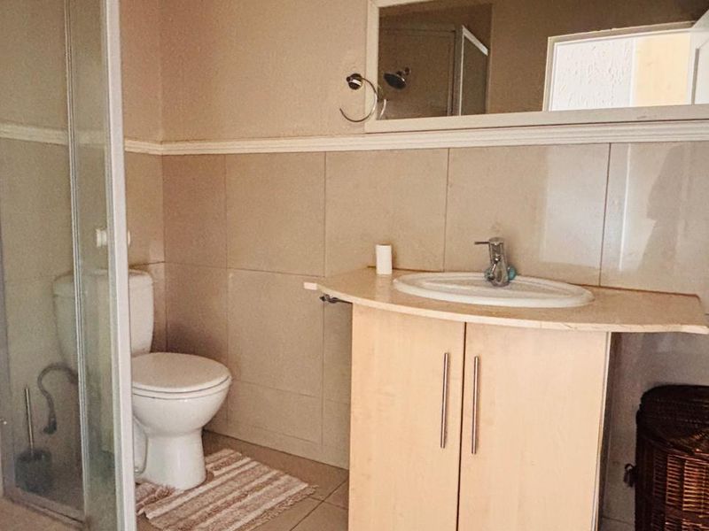 A functional bathroom featuring a shower enclosure, a vanity cabinet with a washbasin, and wall-mounted mirror with neutral tiled finishes.