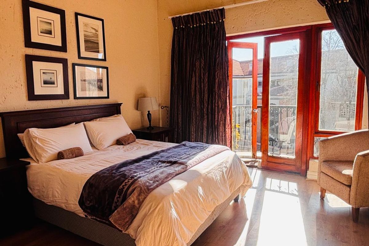 A bedroom featuring laminate flooring and timber-framed glass doors providing direct access to a private balcony.
