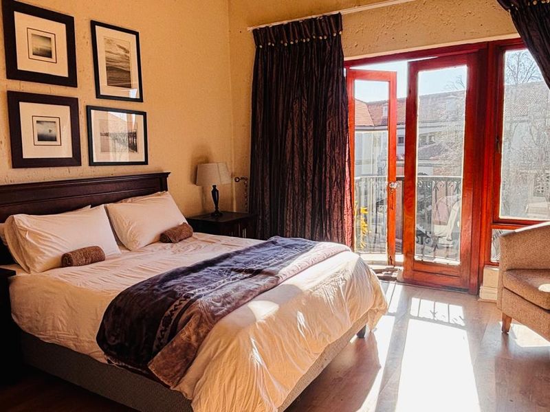 A bedroom featuring laminate flooring and timber-framed glass doors providing direct access to a private balcony.