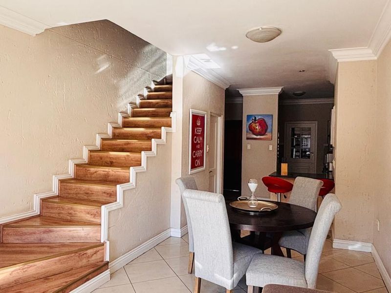 Open plan living area featuring a wooden staircase with white trim and neutral tiled flooring, leading towards a kitchen space.