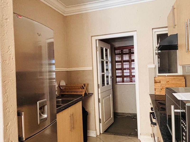 Functional kitchen featuring light wood cabinetry, dark laminate countertops, integrated extractor fan, and tiled flooring, with direct access to an adjacent utility area.