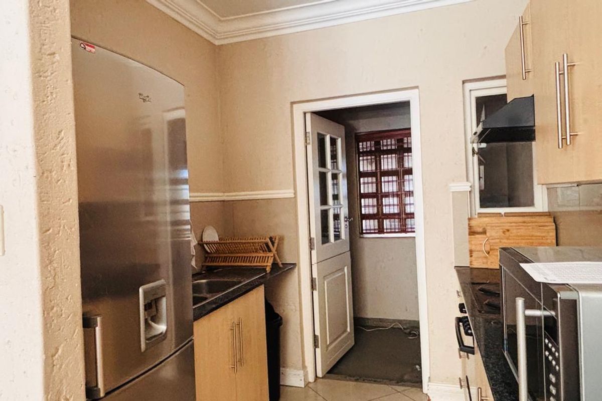 Functional kitchen featuring light wood cabinetry, dark laminate countertops, integrated extractor fan, and tiled flooring, with direct access to an adjacent utility area.