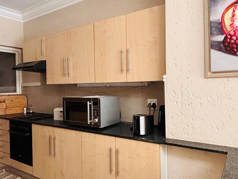 A functional kitchen featuring light wood-finish cabinetry, dark stone-look countertops, and built-in cooking appliances including an oven and extractor fan.