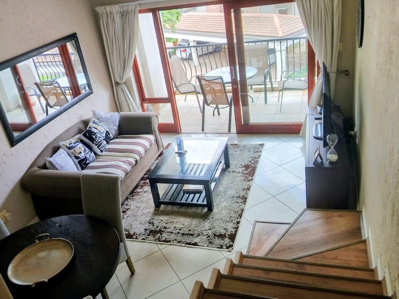 A living room area featuring tiled flooring, a wooden staircase, and a sliding glass door leading to a private balcony.