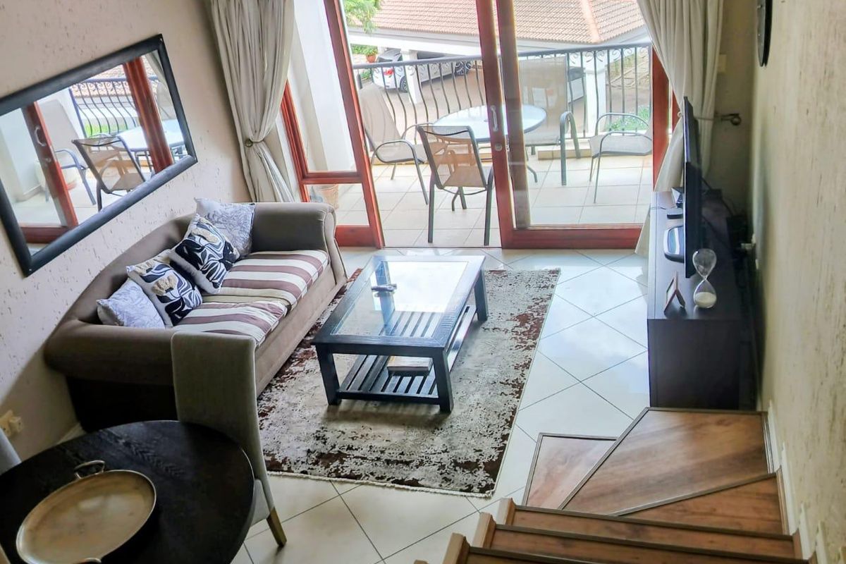 A living room area featuring tiled flooring, a wooden staircase, and a sliding glass door leading to a private balcony.